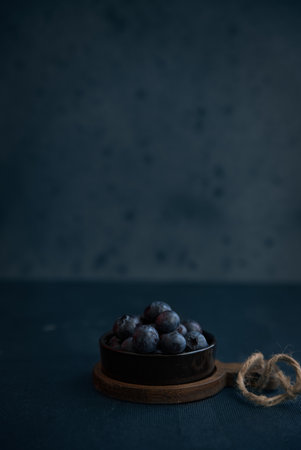 A vertical shot of blackberries in a dark small bowl placed on top of a wooden boardの写真素材