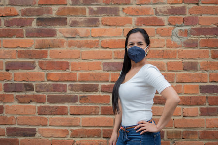 A young Hispanic female with a white shirt and denim pants wearing a protective face mask agの写真素材