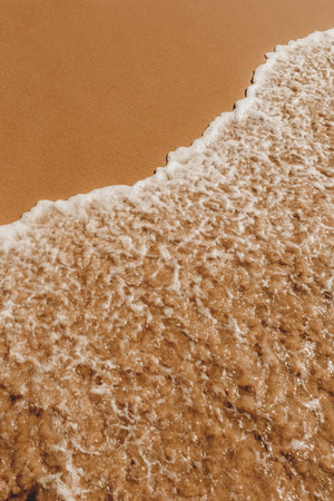 A top view of foam waves hitting a sandy seashoreの写真素材