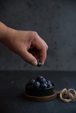 A beautiful closeup shot of a person holding a single blueberry above the pile in the bowlの写真素材