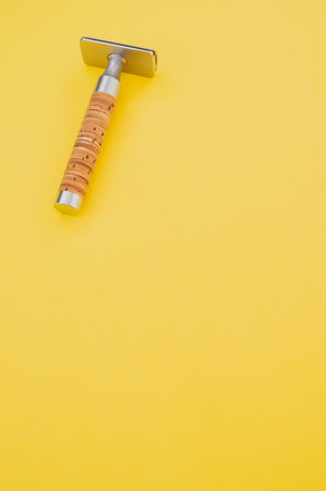 A vertical shot of a t shaped shaving razor on a yellow backgroundの写真素材