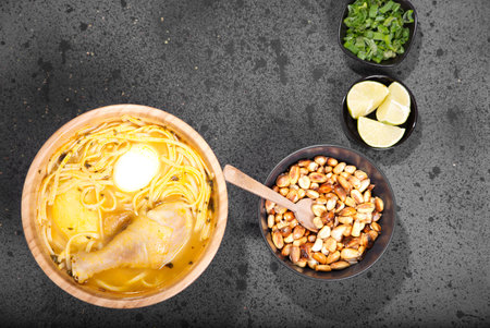 A top view closeup of a Peruvian chicken soup in a wooden bowl with nuts,  lemon, and chivesの写真素材