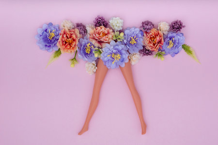 The slender doll legs with artificial flowers on pink background