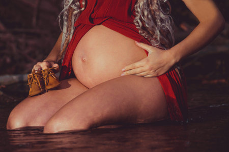 A selective focus shot of a pregnant female holding baby shoes
