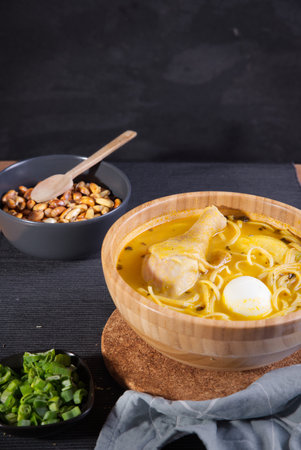 A vertical closeup of a Peruvian chicken soup in a wooden bowl with nuts,  and chivesの写真素材