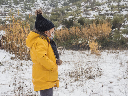 A Caucasian girl with a face mask playing in a snowy fieldの写真素材