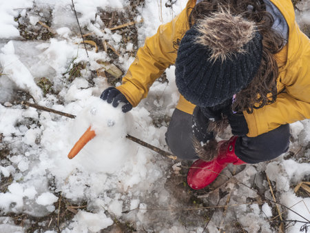 A girl with a hat and gloves making a snowmanの写真素材