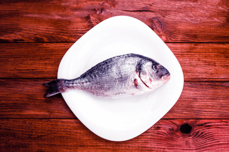 A top view of a raw fish on a white plate and wooden table