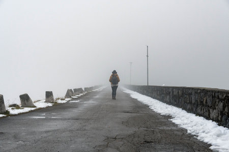 A tourist with a backpack walking on an old stone bridge in a misty weather