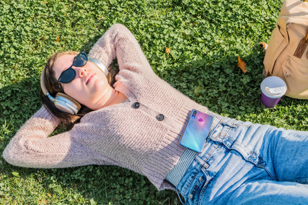 A top view of a female with headphones listening to music and in a park on a sunny day