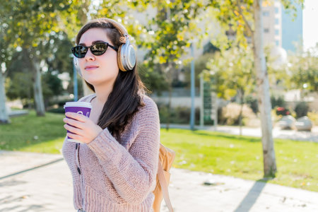 A woman with headphones listening to music and drinking coffee sitting in a parkの写真素材