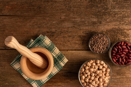 A top view of a mortar with pestle made of wood, 3 bowls of chickpea, red beans, lentil on the tableの写真素材