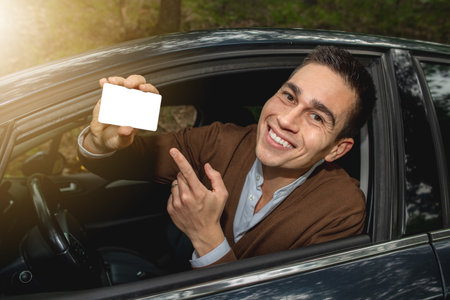 A Caucasian man sitting in the car smiling and holding a white paper with a copy spaceの写真素材