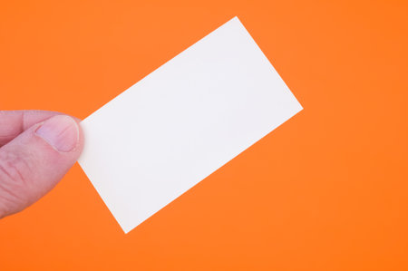 A closeup shot of a person holding a blank paper on an orange backgroundの写真素材