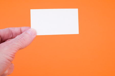 A closeup shot of a person holding a blank paper on an orange backgroundの写真素材