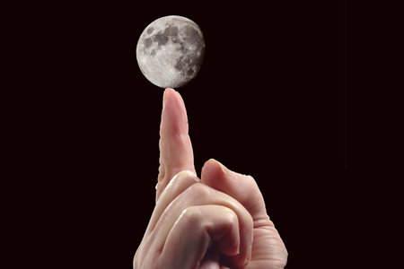 An index finger pointing/supporting/holding the moon on the dark black backgroundの写真素材
