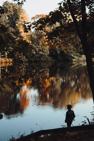 A vertical shot of a person on the bay of a lake reflecting colorful trees in an autumn forest