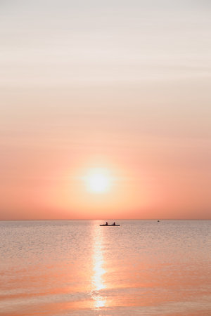 A vertical shot of people in a boat in the calm sea during a scenic sunsetの写真素材