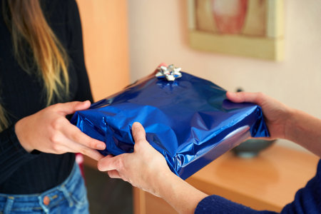 A selective focus shot of a female giving a gift with blue packaging to another femaleの写真素材