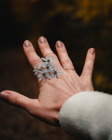 A vertical shallow focus shot of chamomiles on a female's hand with ringsの写真素材