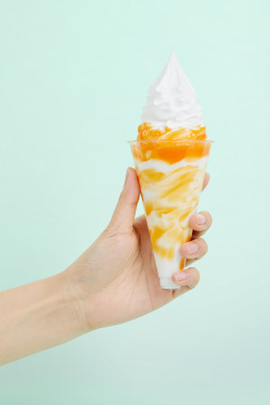 A female's hand holding delicious soft ice cream with topping in a transparent cup on blue backgroundの写真素材