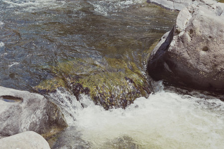 The clear water flowing on the rocks in the river in a park