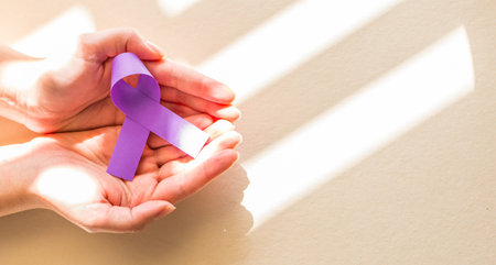 A high angle shot of a female hand holding a purple ribbon on brown background