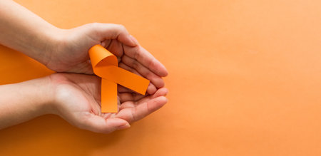 A top view shot of a female hand holding an orange ribbon on orange backgroundの写真素材