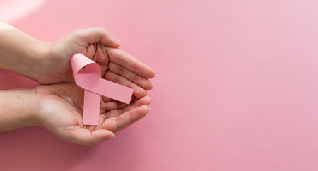 A top view shot of a female hand holding a pink ribbon on pink background