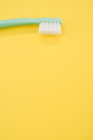 A vertical shot of turquoise toothbrush on a yellow surface for a copy space
