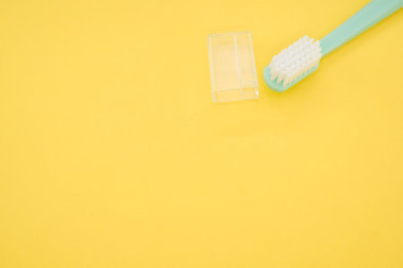 A turquoise toothbrush and a cap cover on a yellow surface for a copy spaceの写真素材