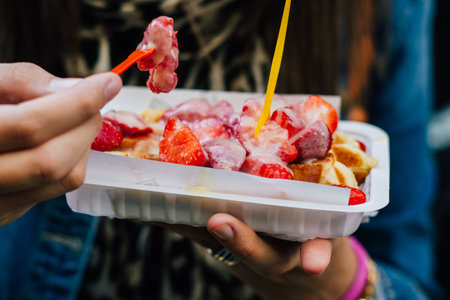A closeup of a person eating Belgian waffles with strawberries in Brusselsの写真素材
