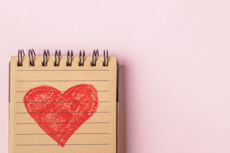 Close-up of a red heart painted in a recycled paper notebook on a pink background. Copy space.の写真素材