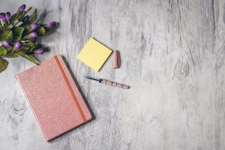 The flat lay of a notebook with a pen, flowers, and stickers on the gray wooden background with copy spaceの写真素材