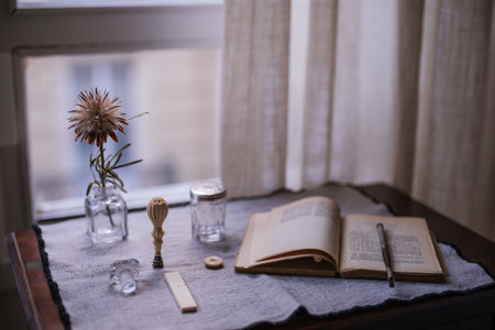 A closeup shot of an opened book near a flower in a vase near the windowの写真素材