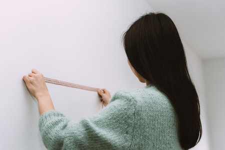 A close shot of a female measuring the wall with a ruler