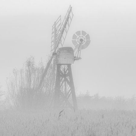 A grayscale shot of a windmill in the field covered with mistの写真素材