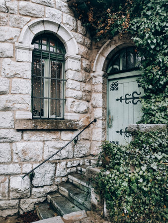 A vertical shot of stairs to the door on an old stone wall house with greenery