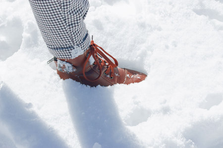 A selective focus shot of a female's foot in the snow, wearing brown leather boots, patterned pantsの写真素材
