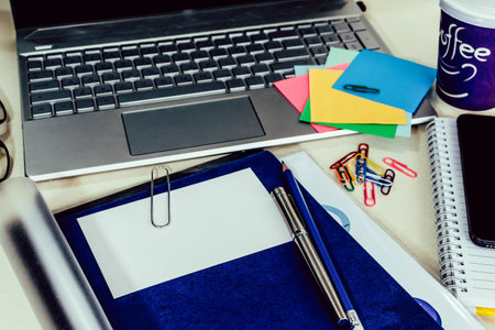 A top view closeup of a laptop, notebook, smartphone, paper clips and a cup of coffee on the desk