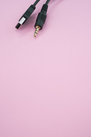 A vertical shot of a USB aux cable isolated on a pink background