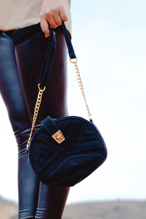 A vertical shot of a female with leather pants holding a velvet fashionable bagの写真素材