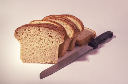 A closeup shot of sliced bread with a knife on white background