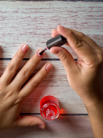 A vertical shot of a woman applying a red treatment oil for nailsの写真素材