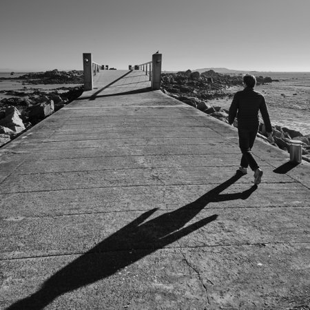 A vertical grayscale shot of a male walking on the pier on a sunny day