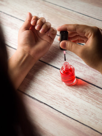 A vertical shot of a woman applying a red treatment oil for nailsの写真素材