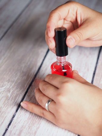 A vertical shot of a woman applying a red treatment oil for nailsの写真素材