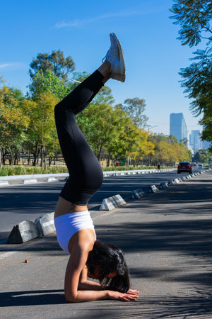 Young person practicing yoga handstand wearing sports clothes, white t-shirt, black pants with urban...