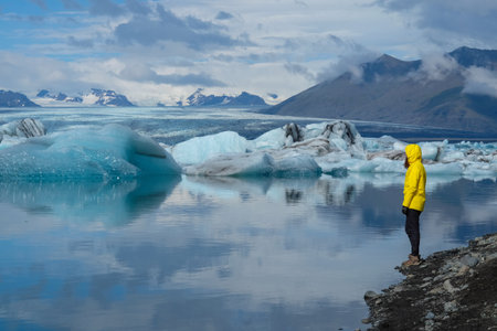 A person with a yellow jacket standing by the sea and enjoying the beautiful view of glaciers in...