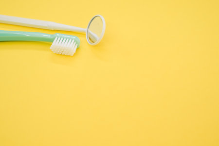 A new green toothbrush and a yellow dental mirror on a yellow backgroundの写真素材